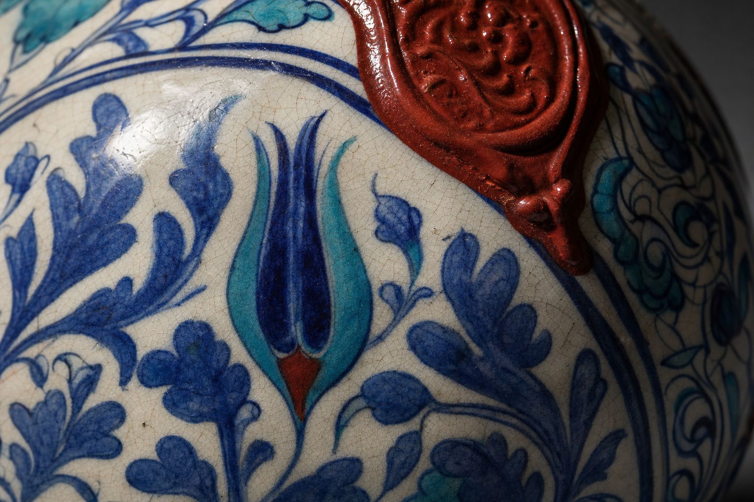 Close detail of glazed ceramic with saz leaves and a tulip in cobalt, turquoise and raised red