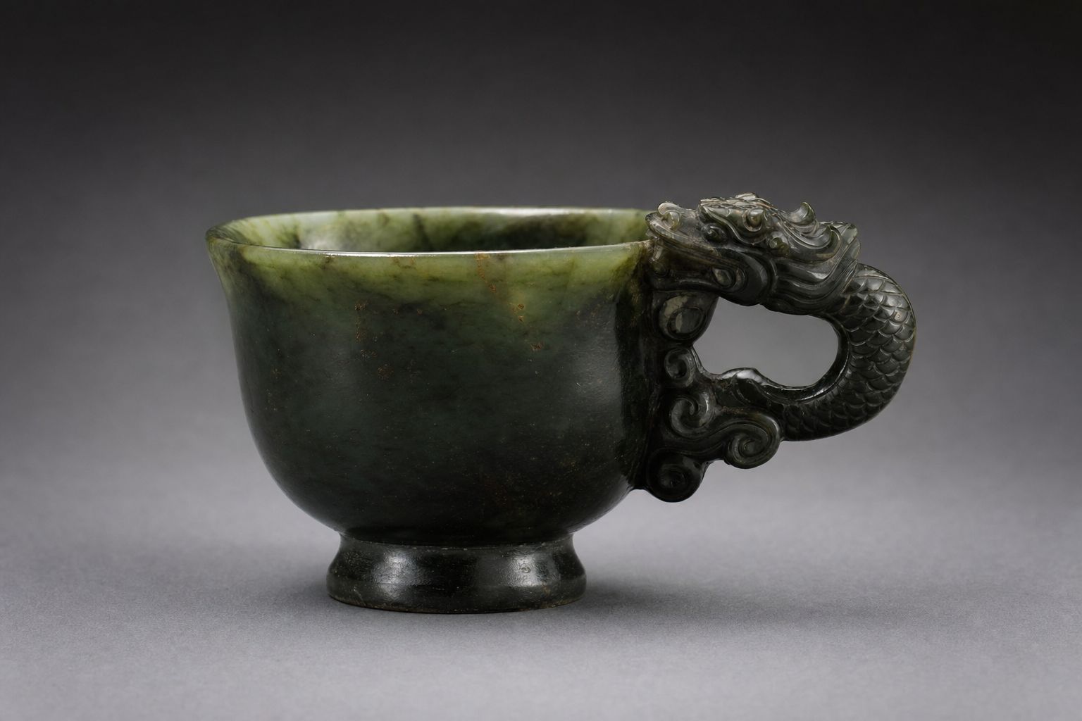 A small footed cup carved from dark green jade with a dragon-shaped handle